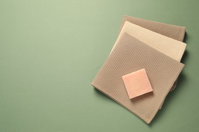 Photo of Clean waffle towels and soap bar on green background, top view. Space for text