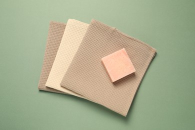 Photo of Clean waffle towels and soap bar on green background, top view
