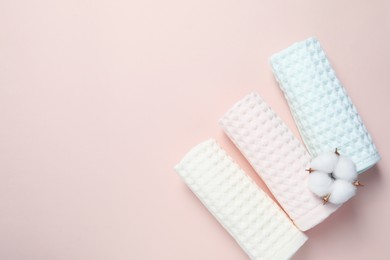 Photo of Clean waffle towels and cotton flower on light pink background, flat lay. Space for text