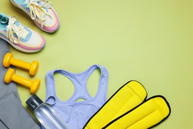 Photo of Sportswear, sneakers, dumbbells, water bottle and ankle weights on green background, flat lay. Space for text