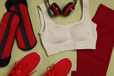 Photo of Sportswear, sneakers, headphones and ankle weights on pale olive background, flat lay