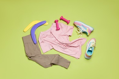 Photo of Sportswear, sneakers, dumbbells and boomerangs on green background, flat lay