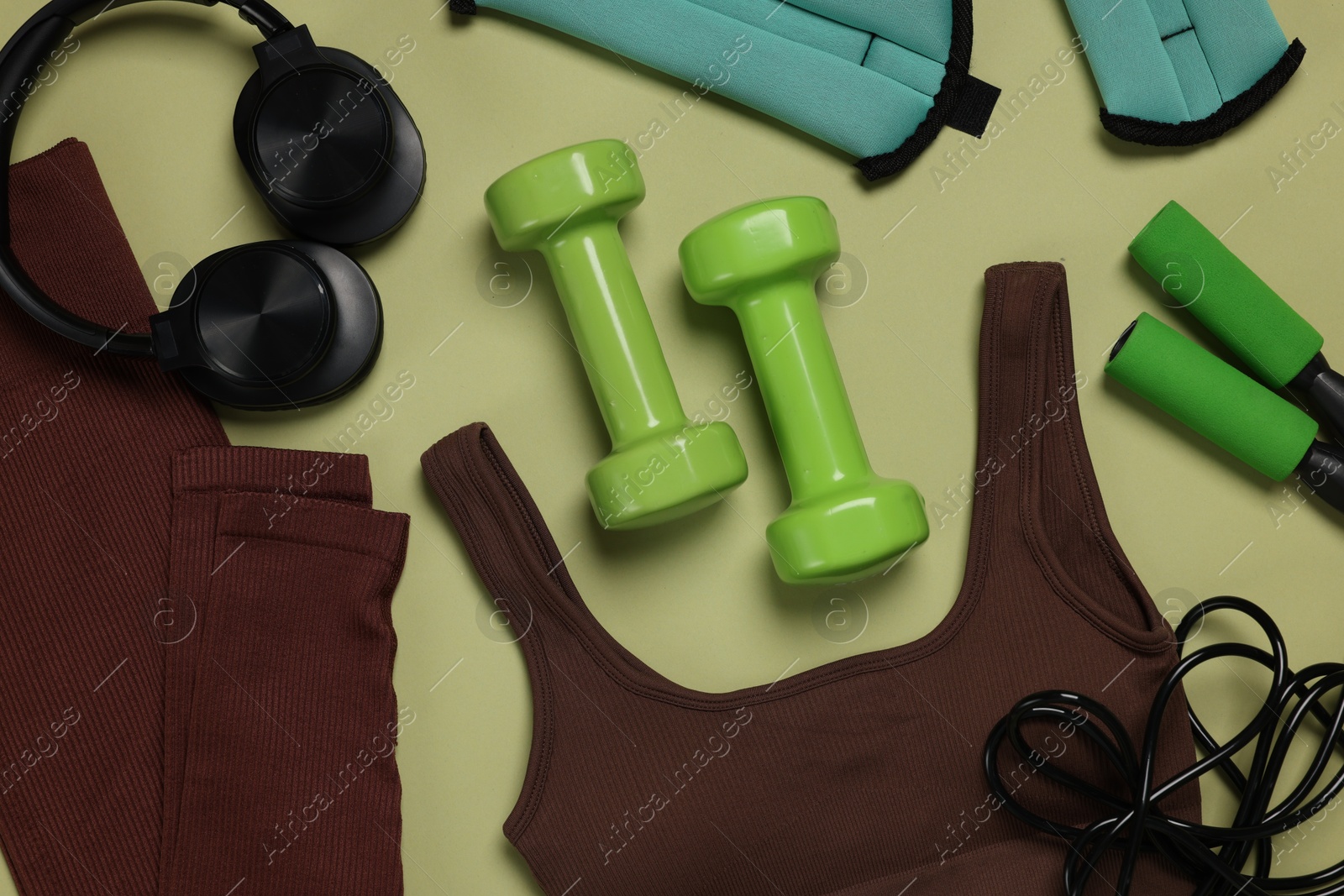 Sportswear, ankle weights, dumbbells, skipping rope and headphones on pale olive background, flat lay Photo of Sportswear, ankle weights, dumbbells, skipping rope and headphones on pale olive background, flat lay
