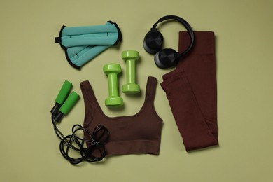 Photo of Sportswear, ankle weights, dumbbells, skipping rope and headphones on pale olive background, flat lay