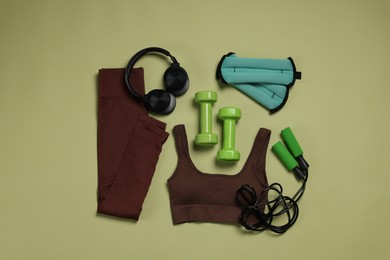 Photo of Sportswear, ankle weights, dumbbells, skipping rope and headphones on pale olive background, flat lay