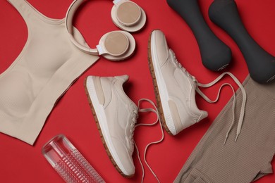 Photo of Sportswear, sneakers, dumbbells, headphones and water bottle on red background, flat lay