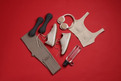 Photo of Sportswear, sneakers, dumbbells, headphones and water bottle on red background, flat lay