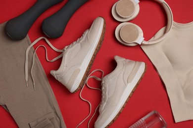 Photo of Sportswear, sneakers, dumbbells, headphones and water bottle on red background, flat lay