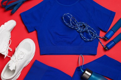 Photo of Sportswear, sneakers, skipping rope and water bottle on red background, flat lay