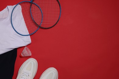 Photo of Sportswear, sneakers, badminton rackets and shuttlecock on red background, flat lay. Space for text