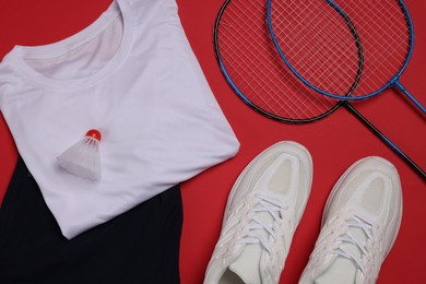 Photo of Sportswear, sneakers, badminton rackets and shuttlecock on red background, flat lay
