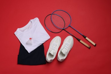 Photo of Sportswear, sneakers, badminton rackets and shuttlecock on red background, flat lay