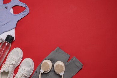 Photo of Sportswear, sneakers, towel, headphones and water bottle on red background, flat lay. Space for text