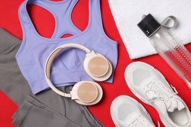 Photo of Sportswear, sneakers, towel, headphones and water bottle on red background, flat lay