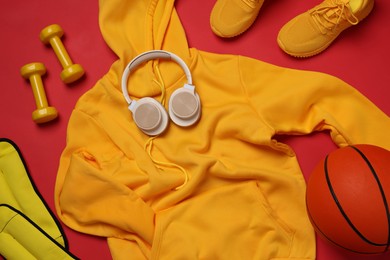 Photo of Sportswear, sneakers, dumbbells, headphones and basketball ball on red background, flat lay