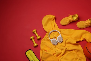 Photo of Sportswear, sneakers, dumbbells, headphones and basketball ball on red background, flat lay. Space for text