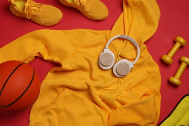 Photo of Sportswear, sneakers, dumbbells, headphones and basketball ball on red background, flat lay