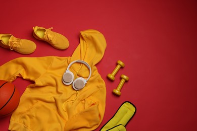 Photo of Sportswear, sneakers, dumbbells, headphones and basketball ball on red background, flat lay. Space for text