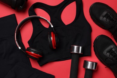Photo of Sportswear, sneakers, dumbbells, headphones and water bottle on red background, flat lay