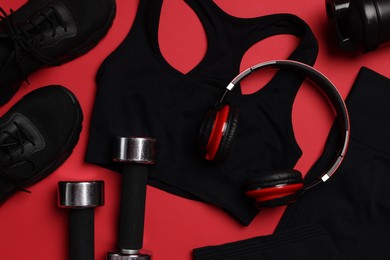 Photo of Sportswear, sneakers, dumbbells, headphones and water bottle on red background, flat lay
