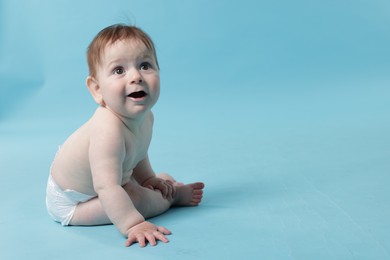 Photo of Cute little baby in diaper sitting on light blue background. Space for text