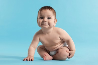 Photo of Cute little baby in diaper sitting on light blue background