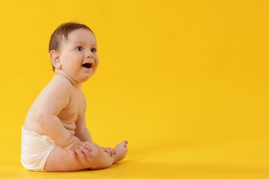 Photo of Cute little baby in diaper sitting on yellow background. Space for text