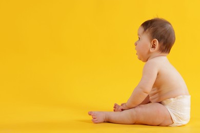 Photo of Cute little baby in diaper sitting on yellow background. Space for text