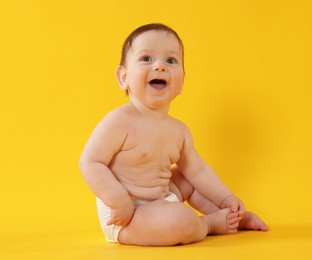 Photo of Cute little baby in diaper sitting on yellow background