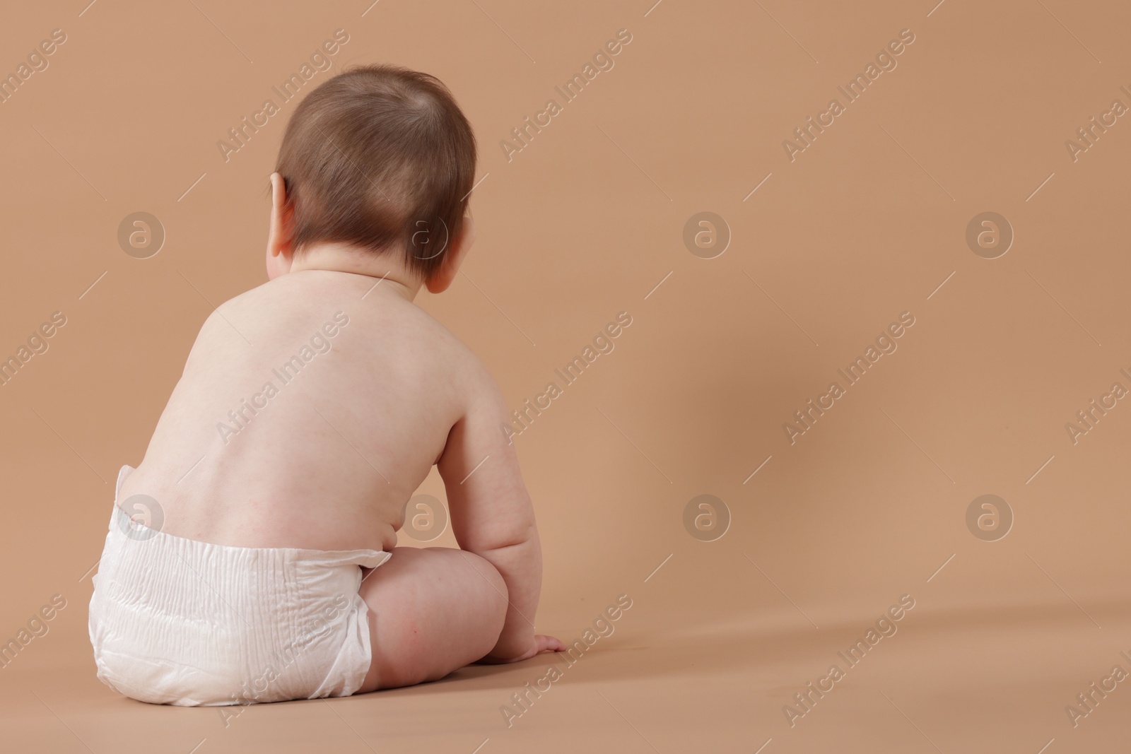 Cute little baby in diaper sitting on beige background, back view. Space for text Photo of Cute little baby in diaper sitting on beige background, back view. Space for text
