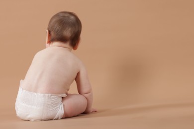 Photo of Cute little baby in diaper sitting on beige background, back view. Space for text