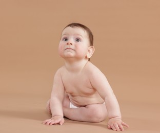 Photo of Cute little baby in diaper sitting on beige background