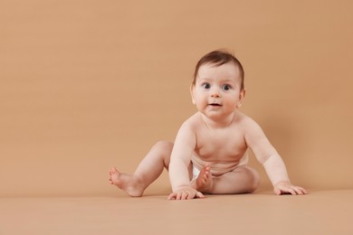 Photo of Cute little baby in diaper sitting on beige background. Space for text