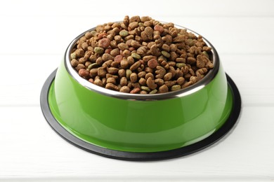 Photo of Dry pet food in feeding bowl on white wooden background, closeup