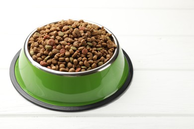 Photo of Dry pet food in feeding bowl on white wooden background, closeup