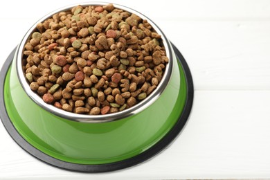 Photo of Dry pet food in feeding bowl on white wooden background, closeup