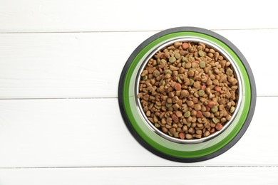 Photo of Dry pet food in feeding bowl on white wooden background, top view. Space for text