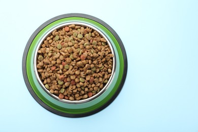 Photo of Dry pet food in feeding bowl on light blue background, top view. Space for text