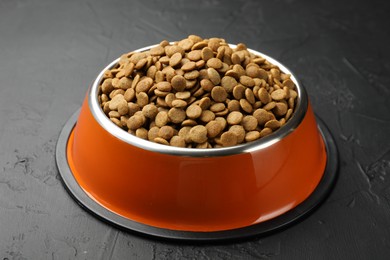 Photo of Dry pet food in feeding bowl on black textured background, closeup
