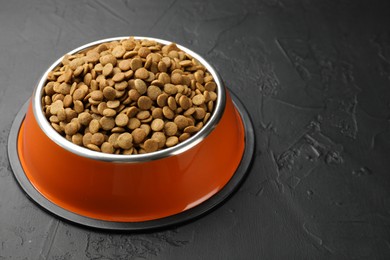Photo of Dry pet food in feeding bowl on black textured background, closeup