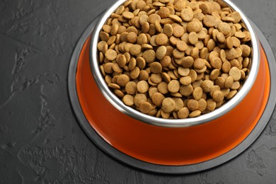 Photo of Dry pet food in feeding bowl on black textured background, closeup