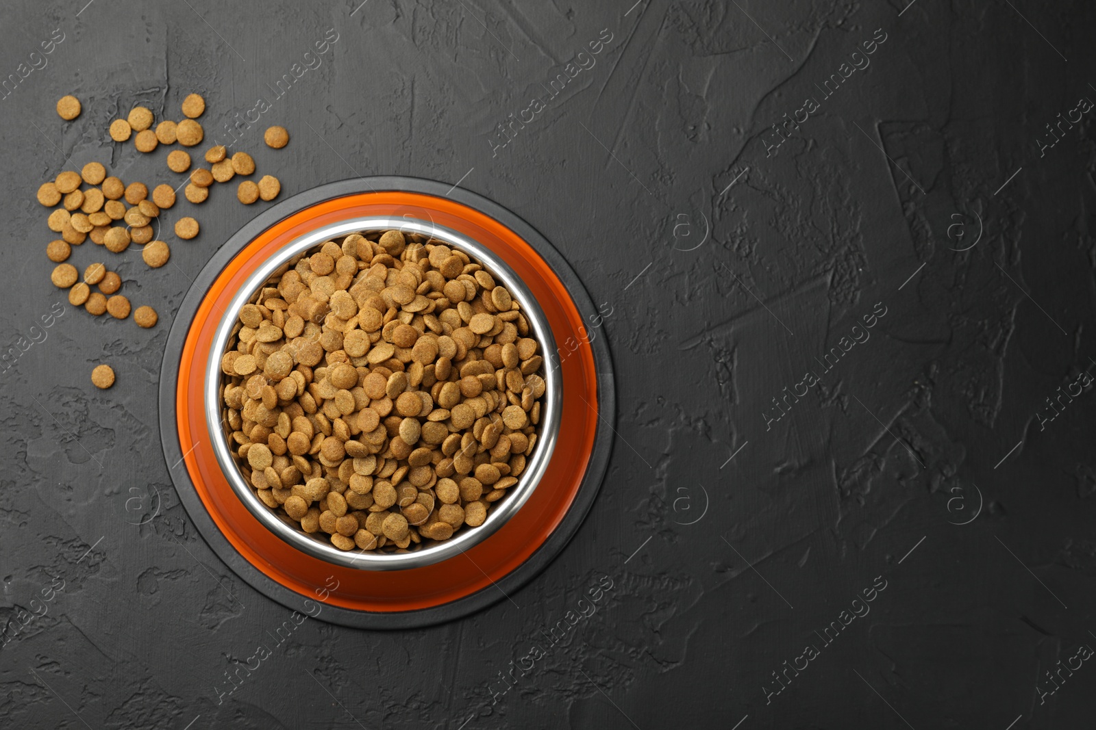 Dry pet food in feeding bowl on black textured background, top view. Space for text Photo of Dry pet food in feeding bowl on black textured background, top view. Space for text