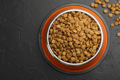Photo of Dry pet food in feeding bowl on black textured background, top view