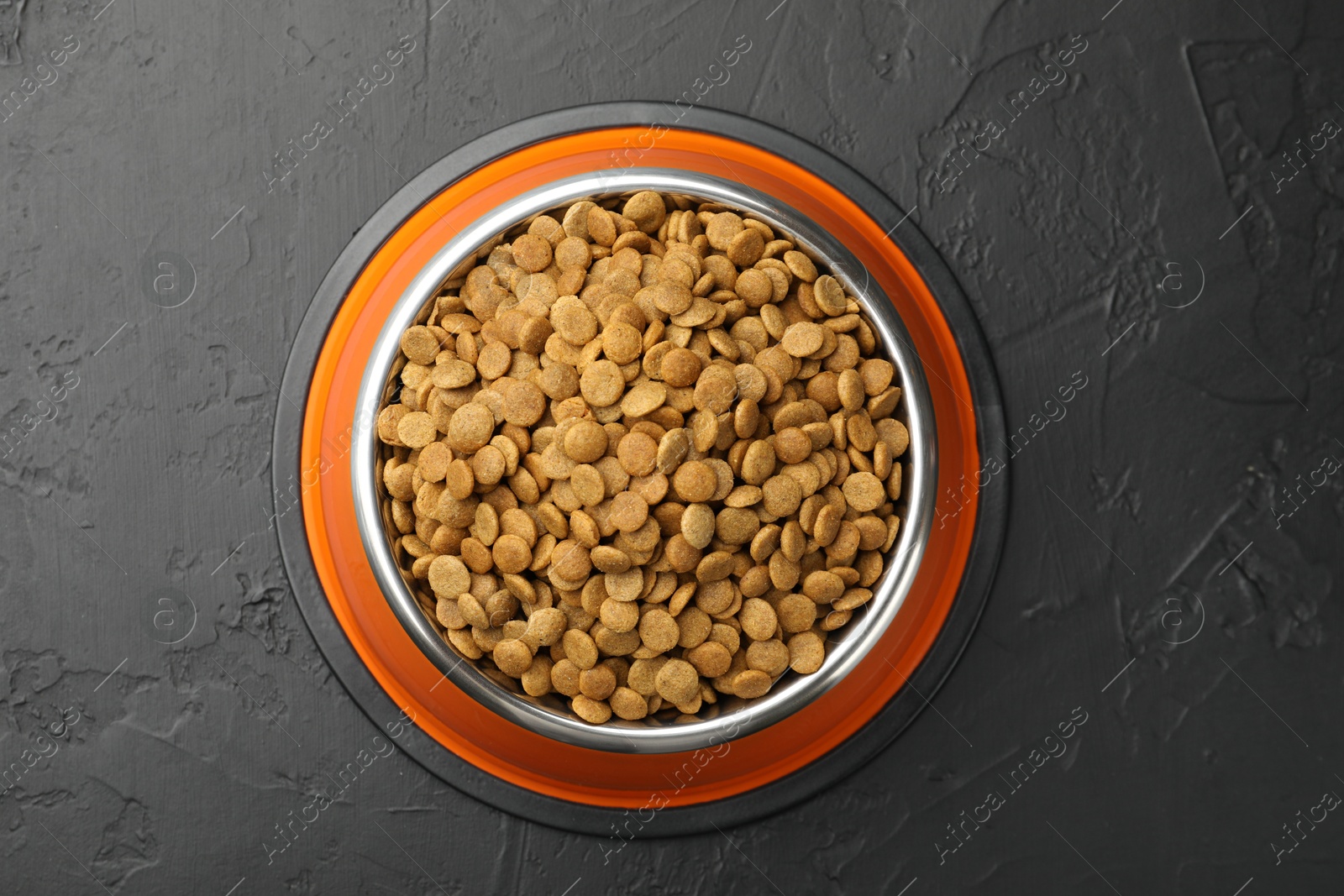 Dry pet food in feeding bowl on black textured background, top view Photo of Dry pet food in feeding bowl on black textured background, top view