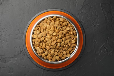 Photo of Dry pet food in feeding bowl on black textured background, top view
