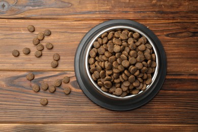 Photo of Dry pet food in feeding bowl on wooden background, top view