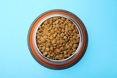 Photo of Dry pet food in feeding bowl on light blue background, top view
