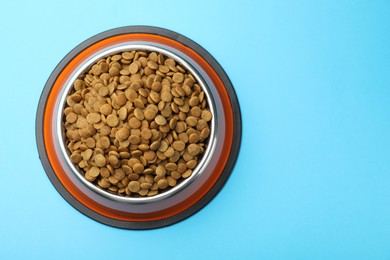 Photo of Dry pet food in feeding bowl on light blue background, top view. Space for text