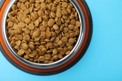 Photo of Dry pet food in feeding bowl on light blue background, top view