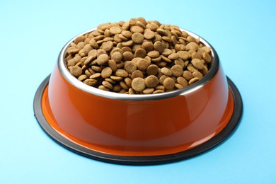 Photo of Dry pet food in feeding bowl on light blue background, closeup